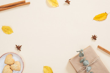Autumn composition. Frame made of dry autumn leaves, gift box, cookies, cinnamon sticks on pastel beige background. Flat lay, top view, copy space
