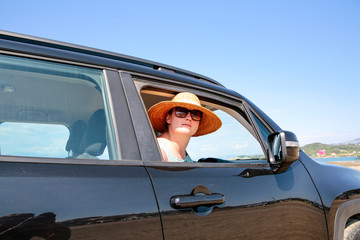 Naklejka premium A woman weraing sunglasses and a hat in the summer car on the beach and ocean view..