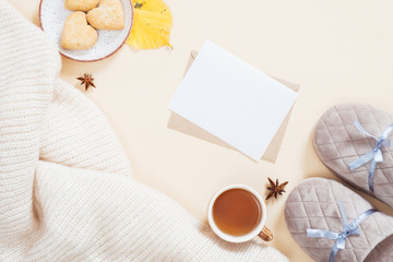 Autumn flatlay composition. Feminine desktop with white knitted plaid, letter, gift box, slippers, tea cup, fallen leaves on pastel beige background. Flat lay, top view. Autumn, fall concept.