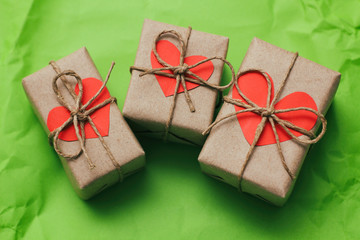 Set of three gift boxes tied with a rope on green crumbled paper background. Carton hearts cards. 