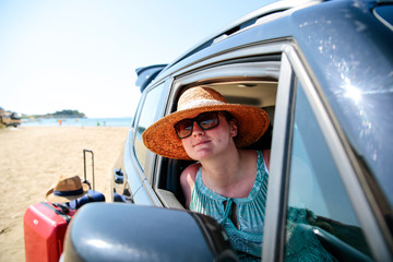 Naklejka premium A woman weraing sunglasses and a hat in the summer car on the beach and ocean view..