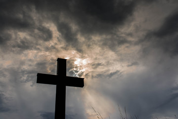 Silhouette of a simple catholic cross, dramatic stormclouds after heavy rain, copy space.