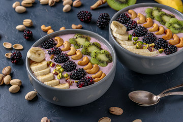 Healthy breakfast smoothie bowl with blackberries, bananas, cashews, kiwi and pistachios on a dark background, horizontal photo