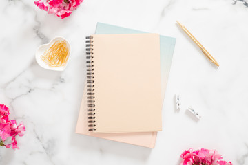 Blank paper notebook, pink flowers and golden stationery on marble background. Flat lay, top view modern home office desk. Fashion blogger workspace concept.