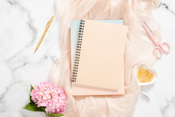 Modern home office desk workspace with pink hydrangea flower, pastel blanket, blank paper notepad, golden stationery and feminine accessories on marble background. Fashion blogger workplace concept.