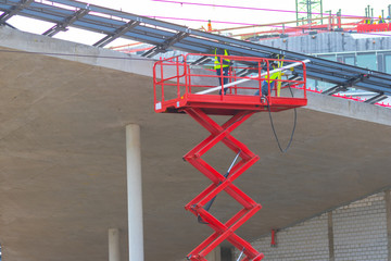 Bauarbeiter, Architekten und Ingenieure begutachten einen Rohbau aus Beton und Stahl mit einer roten Hebebühne / einem roten Baukran in luftiger Höhe