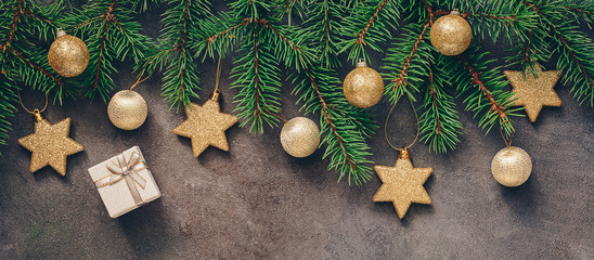 Christmas festive border, branch fir decorated with golden balls and stars, gift box, dark rustic background. Top view, flat lay.