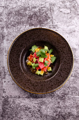 Top view raw tuna salad tartare with cucumber served on a black elegant plate on concrete background. Close up, table restaurant. Easy food for guests.