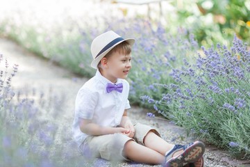 A little boy of 5 years old walks in a flowered park. Lavender. Spring. Portrait of a boy in a hat with a bow tie.