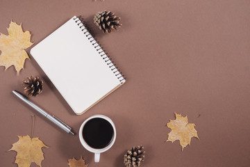 Autumn composition. Golden maple leaves, coffee cup, bumps, notebook and pen on brown background. Autumn or Winter concept. Flat lay, top view