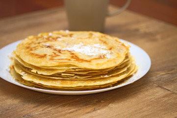 Delicious pancakes with fine icing sugar on a wooden background