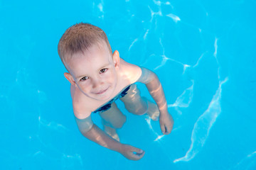 Fototapeta na wymiar Top view of adorable little smiling boy looking at camera while having fun in swimming pool