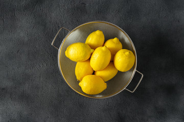 Pile of lemons in colander on a dark background top view