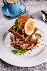 Plate of belgian chocolate waffles with slice orange, ice cream, caramel sauce and fresh mint on elegant white plate on concrete background. Close up. Top view dessert