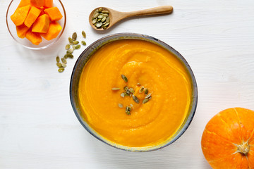 Pumpkin soup with pumpkin seeds on white wood background. Healthy food concept, top view
