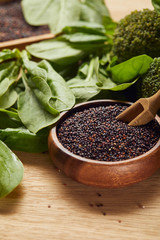 black quinoa seeds in wooden bowl with spatula near green spinach leaves