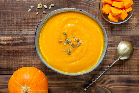Pumpkin soup with pumpkin seeds on dark wood table, top view