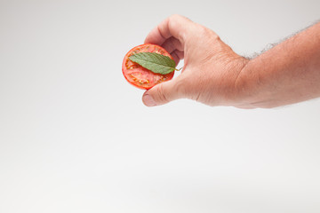 Medio tomate con una hoja de menta en la mano de una persona