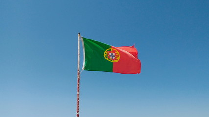 The portuguese flag  (Portugal), in a light blue sunny  sky