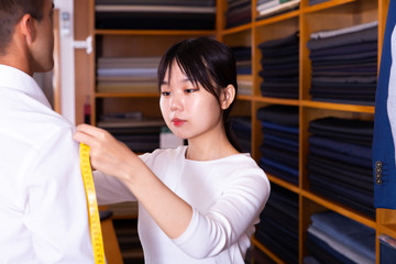 Woman tailor makes measurements of customer clothes in shop