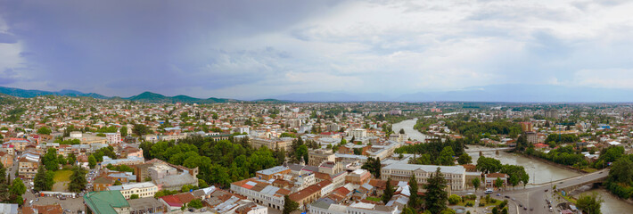 Panoramic summer view of the city of Kutaisi, Georgia. Blue sky with clouds. River Rioni and old houses with Red roofs. Mountains in the distance.
