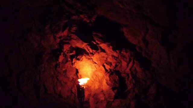 Oil torch burning inside dark natural cave making shadows on cave walls. Filmed while taking a group spring hike in slow motion hd.