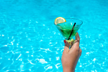 Woman hand with tropical cocktail glass near the swimming pool
