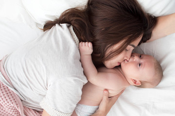 Obraz na płótnie Canvas A brunette woman kisses a baby. Mom with baby closeup