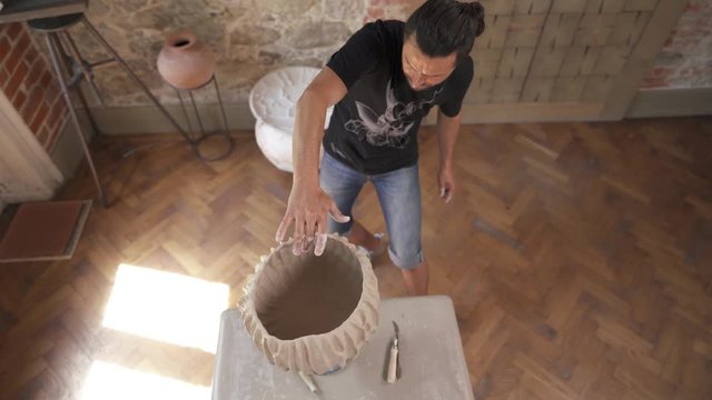 A view of man making ceramics dish on pottery wheel. Potter shapes the clay product - pot - with professional tools, top view. Artist working in workshop