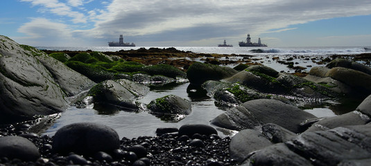 Rocks and water puddles in foreground with the low tide and ships in the background, coast of Las Palmas, Gran Canaria 