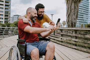 a disabled man on wheelchair with his assistant looking to a mobile phone