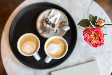 two cups of coffee and a pink rose in a marble table