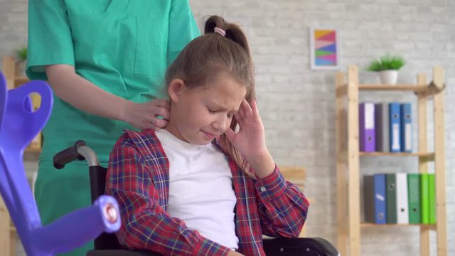 Doctor masseur doing neck massage to a teenage girl in a wheelchair close up
