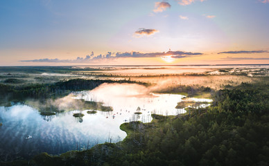 Warmly colored sunrise over a foggy swamp. Aerial view of stunning landscape at peat bog at Cenas...