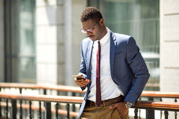 handsome young adult african man in suit and glasses with a phone in his hand