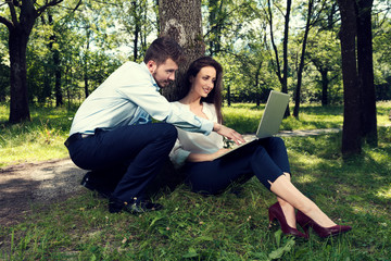 Business man and business woman working on a project together sitting under the tree in a public city park Selective focus
