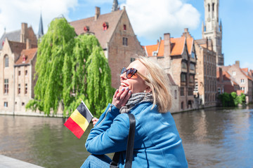 Obraz premium Młoda kobieta z flagą Belgii w dłoniach rozkoszuje się widokiem kanałów w historycznym centrum Brugii.