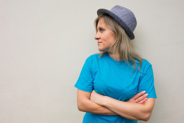 Girl in hat. White middle aged woman looks away and crosses arms on breast. Front portrait with turned head and positive face