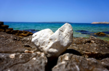 Beautiful summer background with a white heart shaped stone in front of the beautiful blue sea and sky horizon line