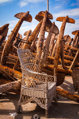 RUSTY ANCHORS AND ABANDONED WICKER CHAIR IN FISHING PORT