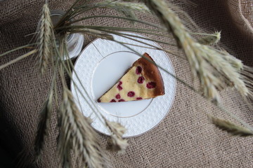 Raspberry cake piece on white plate with background of  sackcloth and spikelet