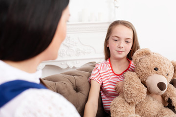 Teen girl on reception at the psychotherapist. Psychotherapy session for children. The psychologist works with the patient. Girl smiling sitting on a sofa next to a sitting female doctor therapist