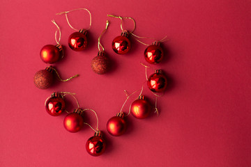 Red Christmas tree decorative toy balls on red celebratory Christmas background laid out in the shape of a heart. New Year's holidays. Christmas holidays