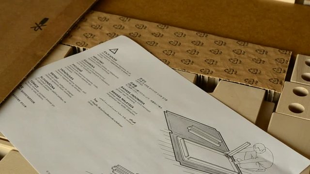 Turin, Piedmont, Italy. July 2019. The hand of a Caucasian man leafs through instructions for mounting the Ikea Norden model table and its newly unpacked components.