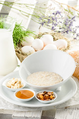 Oatmeal in a beautiful white plate with honey, nuts and banana on light delicate background