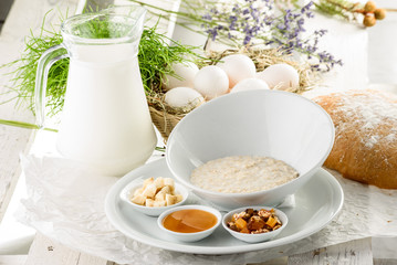 Oatmeal in a beautiful white plate with honey, nuts and banana on light delicate background