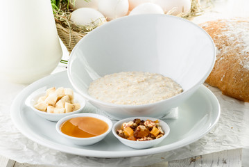 Oatmeal in a beautiful white plate with honey, nuts and banana on light delicate background