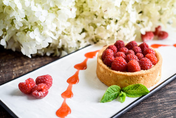 raspberry tart on a white plate on a dark wooden background
