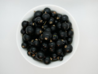 Ripe black currant berries in a small white Cup on a white background. Black currant harvest. Natural vitamin. Healthy food. vegetarian food.