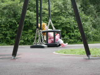 a beautiful doll on a children's swing in a city Park on a Sunny summer day